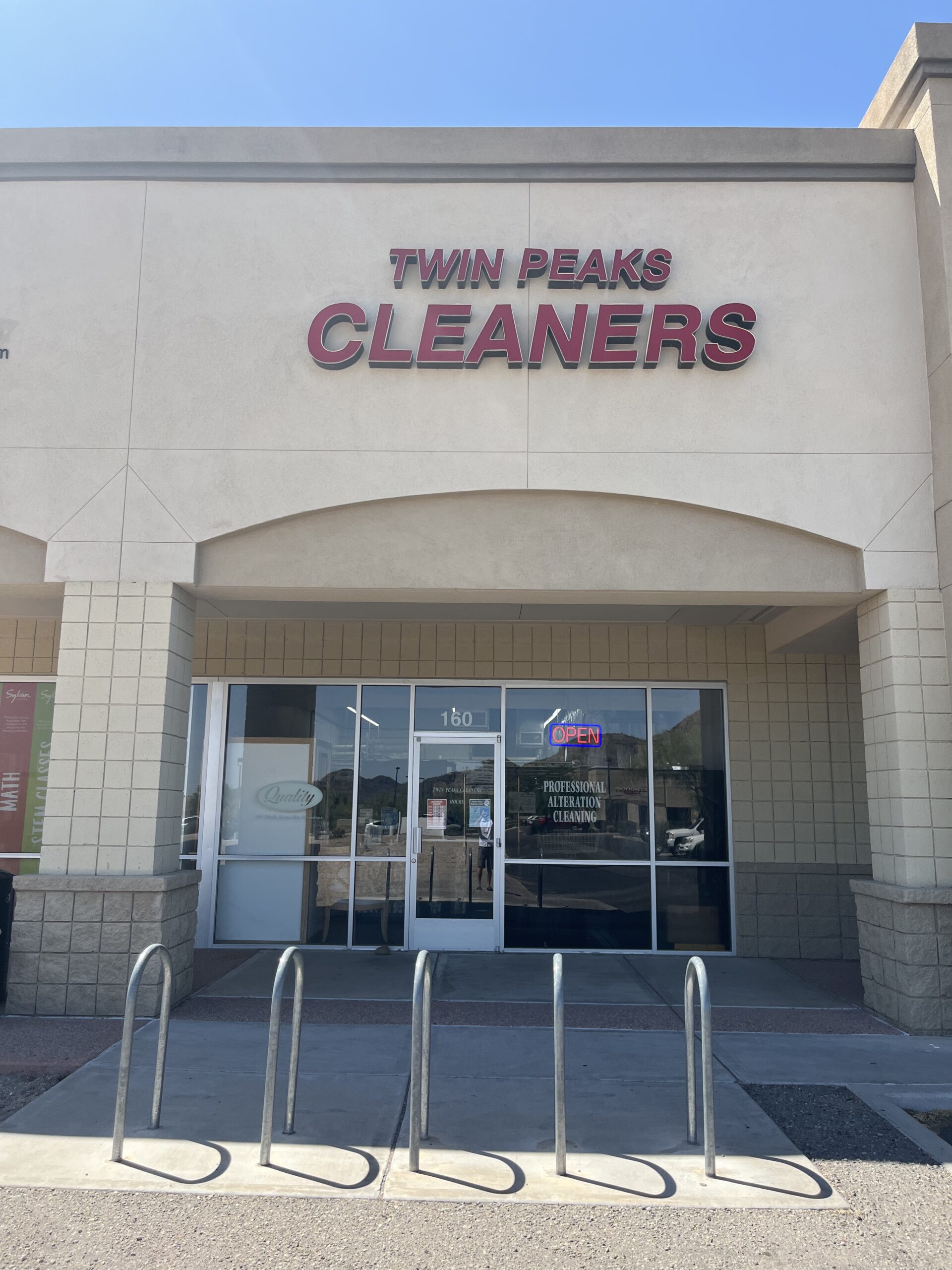 The exterior of Twin Peaks Cleaners, with a glass door, large windows, a bike rack, and an