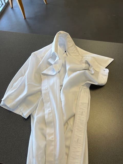 A white button-up shirt lies crumpled and partially folded on a dark tabletop, with the collar and sleeves visible.