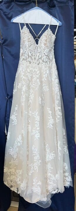 A white sleeveless wedding dress with floral lace patterns hangs on a blue hanger against a blue background.